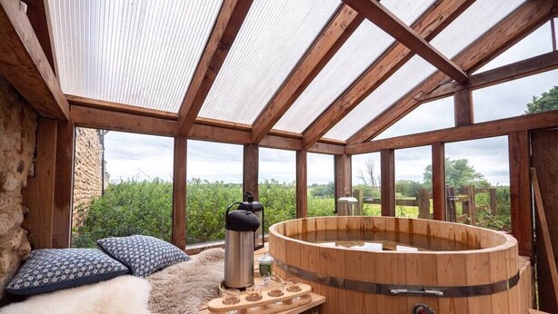 A wooden hot tub with a glass ceiling, a wooden bench with cushions, and a wooden table with a thermos and glasses. - Annex Suite: Sleeps 2 (Scunthorpe)