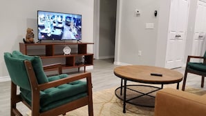 A living room with a television, a wooden coffee table, and green chairs. - The Beaver Den 30 day stays King bed Lake Conroe (Montgomery)