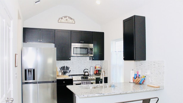 A modern kitchen with dark cabinets, stainless steel appliances, a granite countertop, and a small island with bar stools. - The Beaver Den 30 day stays King bed Lake Conroe (Montgomery)