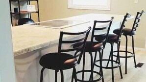 A kitchen with a wooden floor, a white countertop, and four black bar stools. - Completely renovated lakehouse with all the extras (Warsaw)