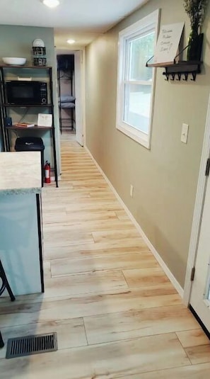 A hallway with wooden flooring, a microwave, a fire extinguisher, and a window with a view.