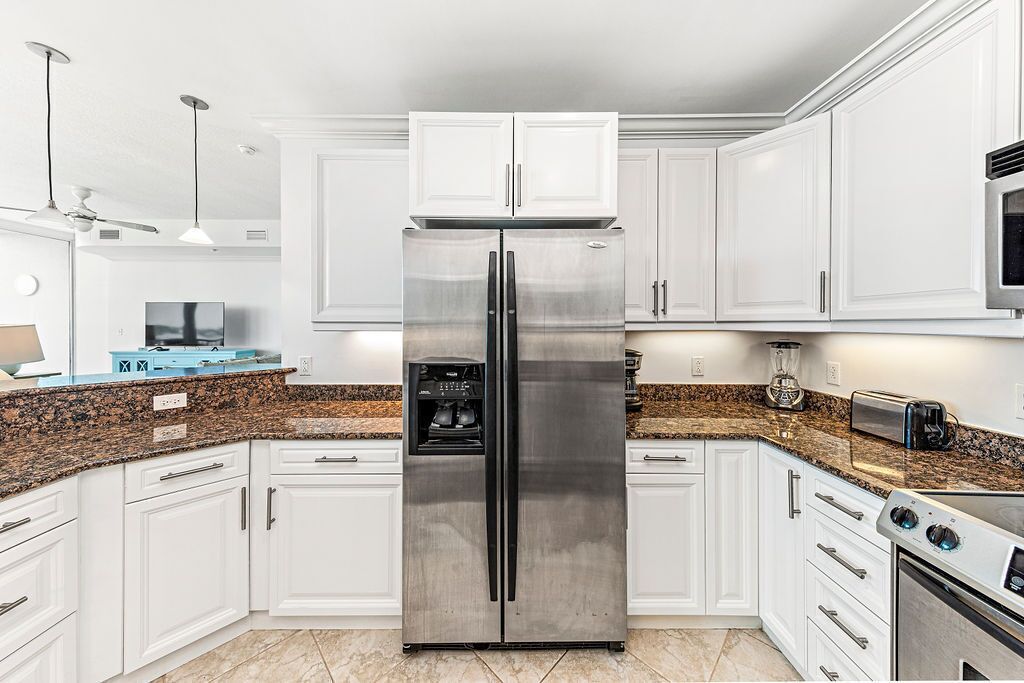 Eine moderne Küche mit weißen Schränken, einem Edelstahl-Kühlschrank, Granit-Arbeitsplatten und einem eingebauten Backofen.