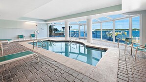 Une piscine intérieure offrant une vue dégagée sur la mer et un espace extérieur aménagé avec des chaises longues.
