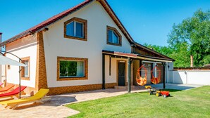 Ein zweigeschossiges Haus mit rotem Ziegeldach, einer Veranda und einem Rasen mit Gartenmöbeln.