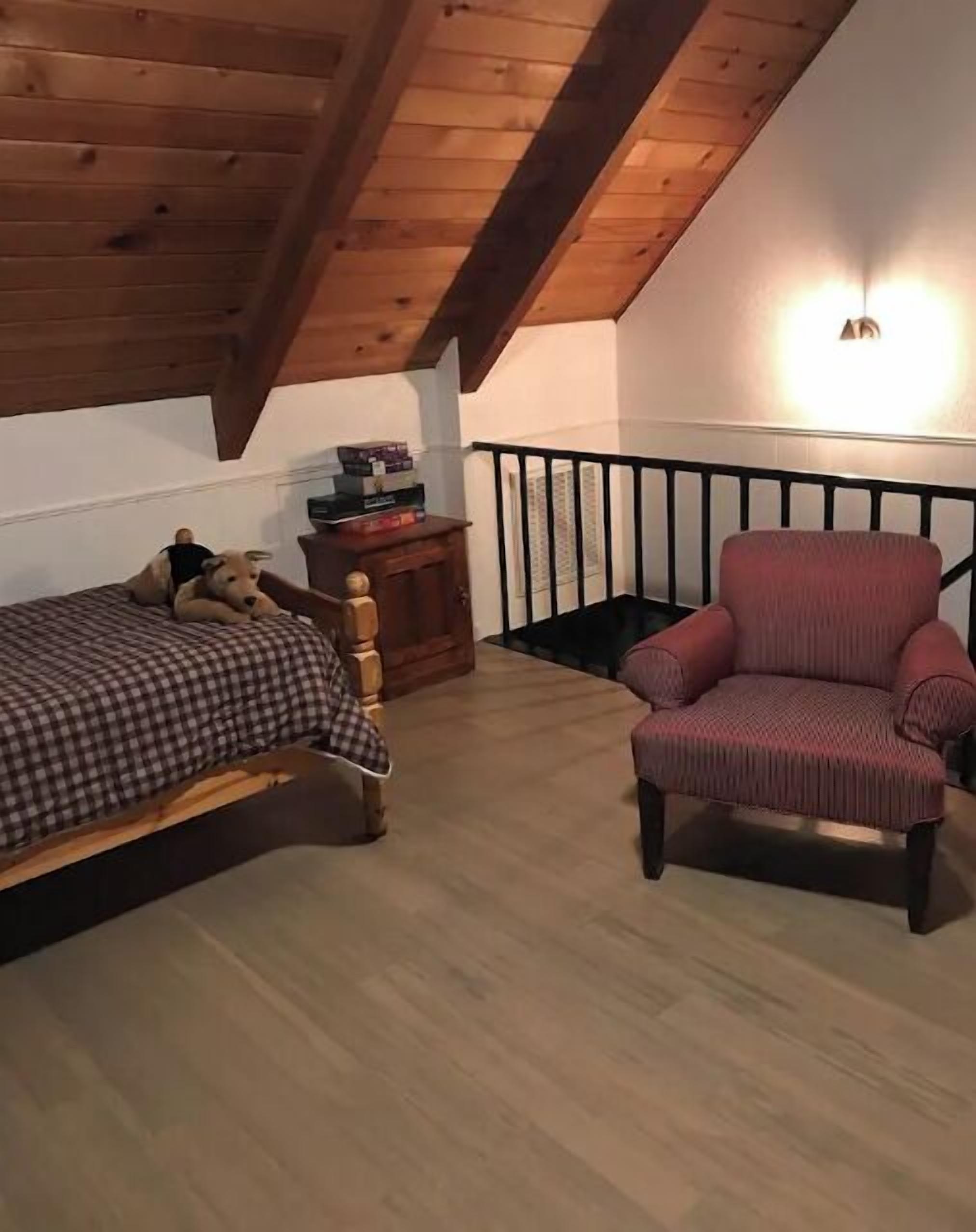 Ein gemütliches Zimmer mit Bett, Stuhl, kleinem Tisch und einer Treppe.