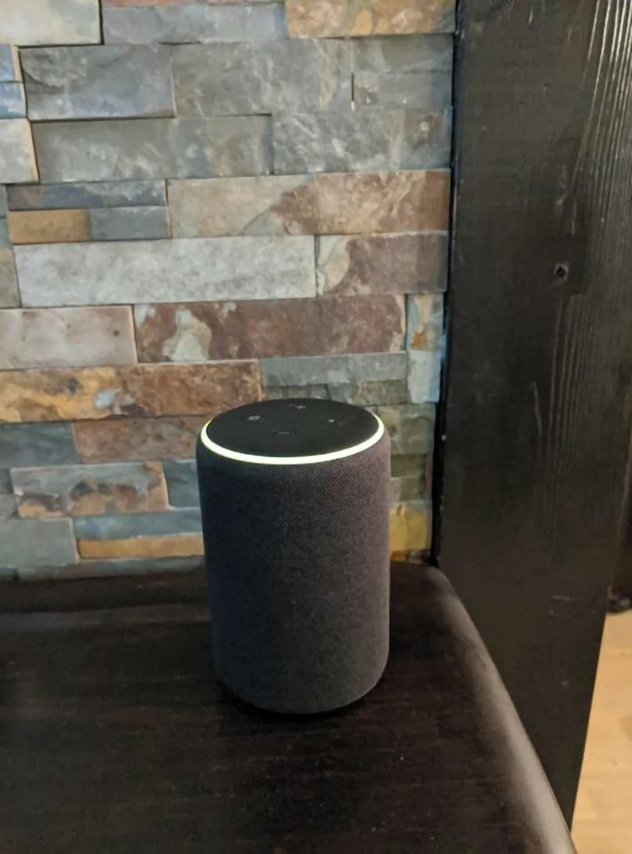 A smart speaker on a black surface against a stone wall.