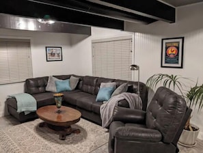 A living room with a dark leather sofa, a round wooden coffee table, a floor lamp, and a potted plant.