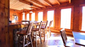 Een rustiek houten interieur met een bar, houten stoelen en grote ramen voor natuurlijk licht.