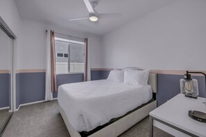 A hotel room with a bed, a desk, a lamp, and a window with curtains. - Breezin': Pool, Spa, Fire Pit, Foosball and more! (Indio)