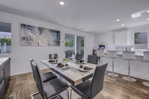 Un espace repas moderne avec une longue table dressée pour six personnes, des chaises noires et un grand tableau abstrait accroché au mur.