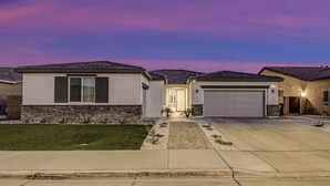 A modern two-story house with a stone facade, a front driveway, and a garage. - Breezin': Pool, Spa, Fire Pit, Foosball and more! (Indio)