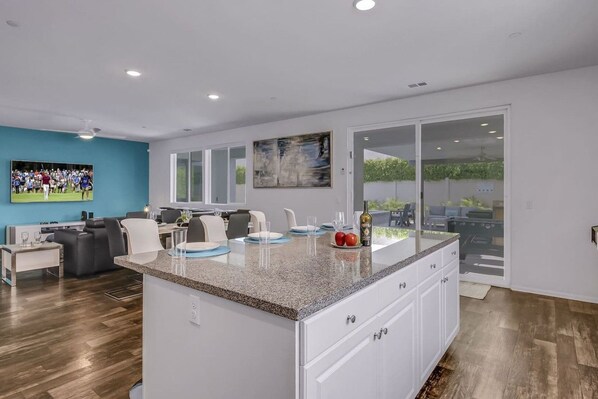 A modern kitchen with a granite countertop, white cabinetry, and a dining area with a table and chairs.