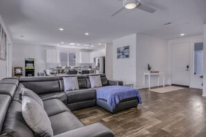 A modern living room with a sectional sofa, a small table, and a ceiling fan. - Breezin': Pool, Spa, Fire Pit, Foosball and more! (Indio)