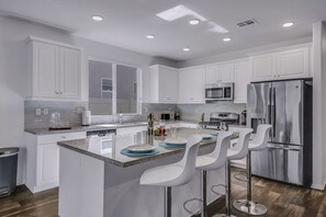 A modern kitchen with white cabinetry, stainless steel appliances, and a central island with bar stools.