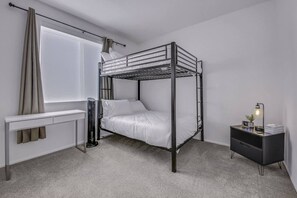A bunk bed with a desk and a nightstand in a room with a window and curtains.
