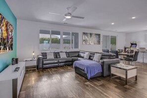 A modern living room with a sectional sofa, a coffee table, and a dining area with a table and chairs. - Breezin': Pool, Spa, Fire Pit, Foosball and more! (Indio)