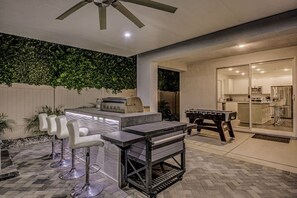 An outdoor patio with a bar area, seating, and a foosball table. - Breezin': Pool, Spa, Fire Pit, Foosball and more! (Indio)