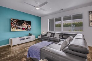 A modern living room with a grey leather sofa, a white entertainment unit, and a large TV displaying a sports event.