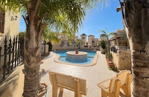 A pool area with a circular fountain, surrounded by stone walls and palm trees.