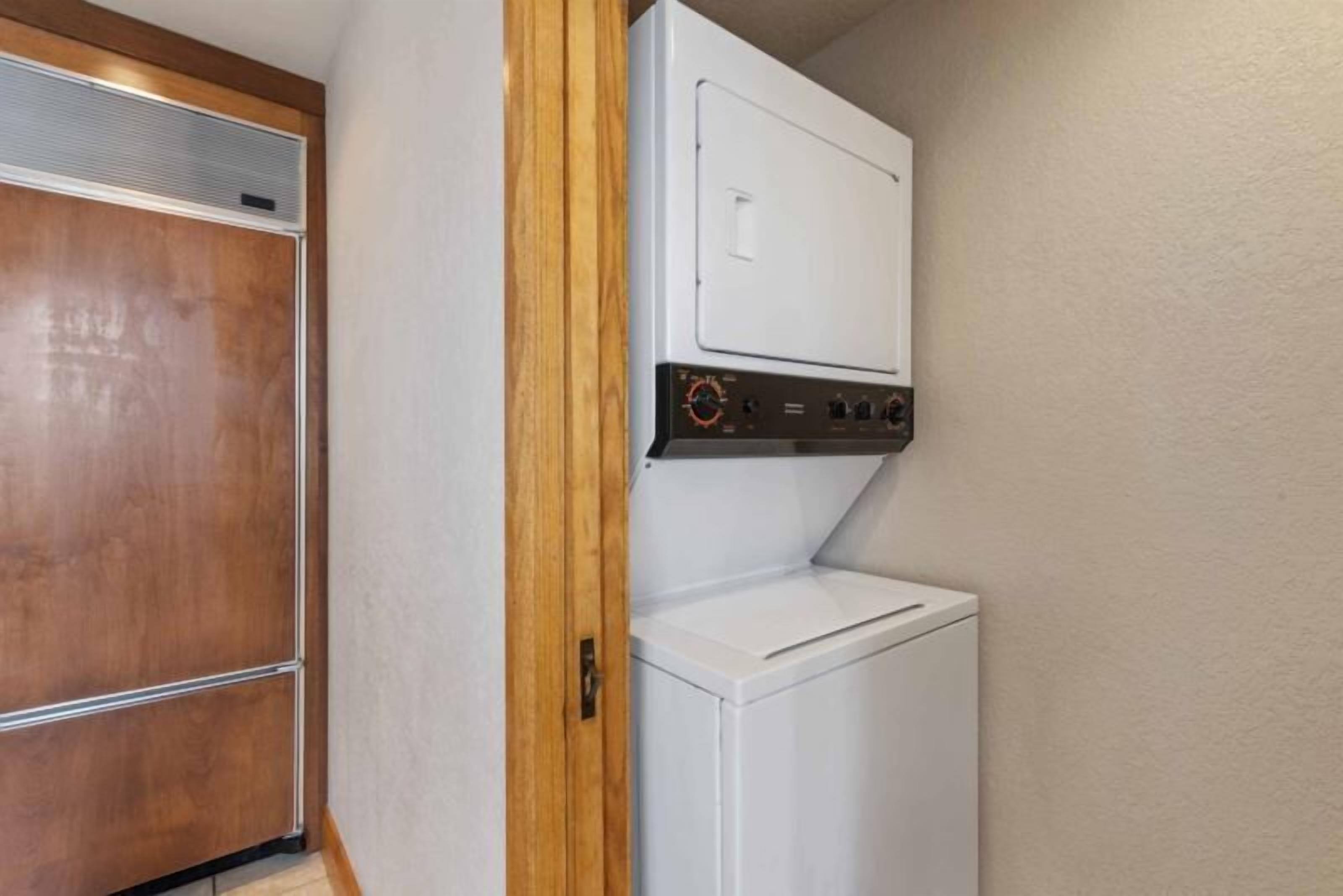 A compact laundry room with a built-in washer and dryer, wooden door, and a small countertop.