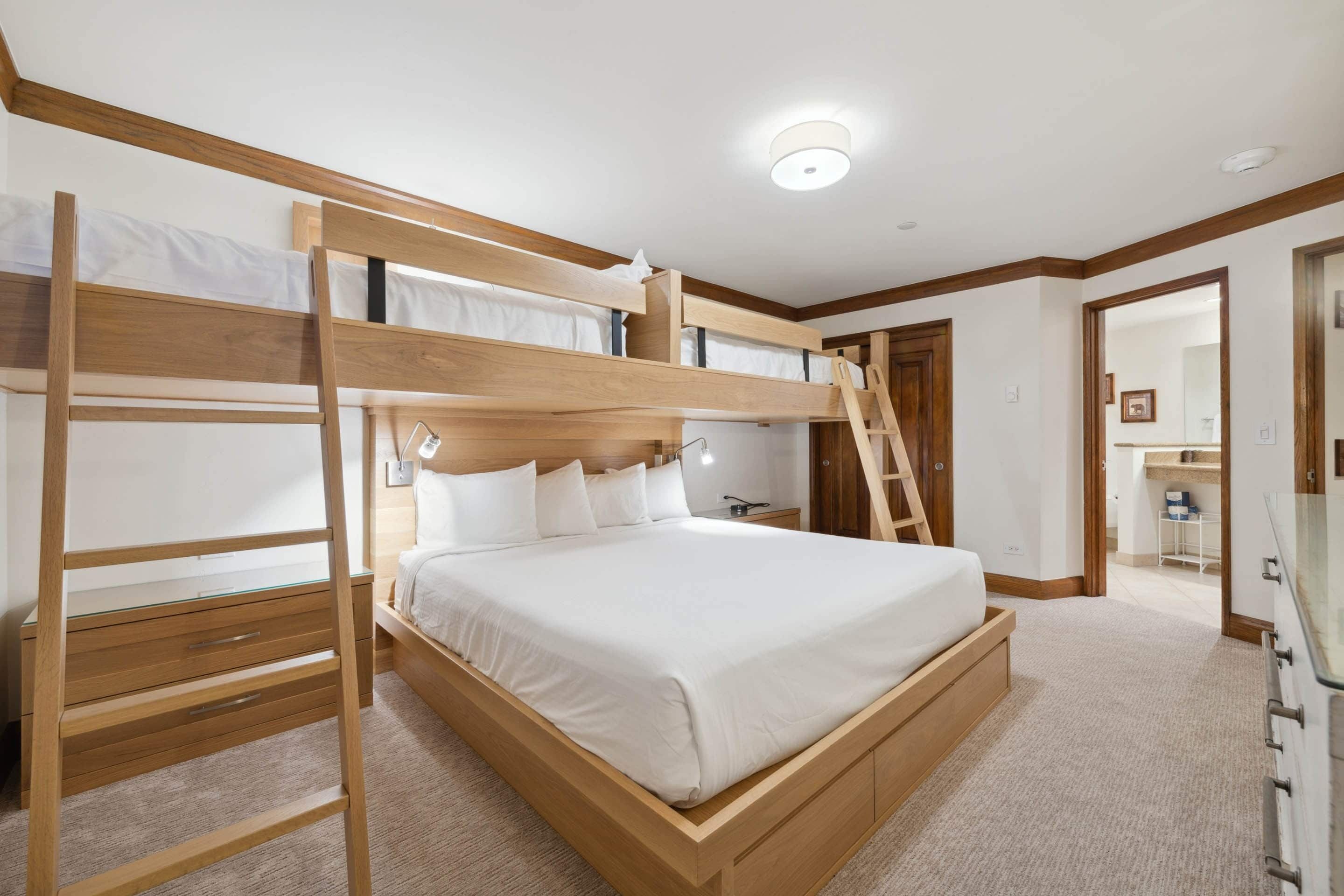 A bunk bed room with a wooden ladder, a bedside table, and a nightstand.