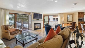 A spacious living room with a fireplace, comfortable seating, a glass coffee table, and a view of the outdoors. - The Charter at Beaver Creek L032 (Beaver Creek)