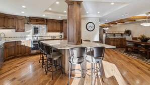 A spacious kitchen with wooden cabinets, a large island with bar stools, and a clock on the wall. - The Charter at Beaver Creek L032 (Beaver Creek)