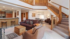 A spacious living area with a wooden staircase, a sofa set, and a kitchen area. - The Charter at Beaver Creek L011 (Beaver Creek)