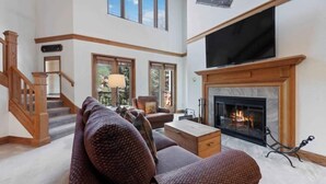A spacious living room with a fireplace, a large TV mounted above it, and a staircase leading to an upper level. - The Charter at Beaver Creek L011 (Beaver Creek)