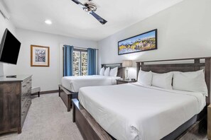 A hotel room with two beds, a desk, a TV, and a painting on the wall.