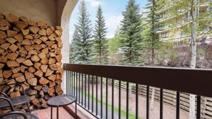 A balcony with a stack of firewood, metal chairs, and a view of tall evergreen trees. - The Charter at Beaver Creek A210 (Beaver Creek)