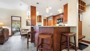 A modern kitchen with wooden cabinets, a central island with stools, pendant lighting, and a view of the dining area. - The Charter at Beaver Creek A210 (Beaver Creek)