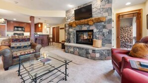 A cozy living room with a stone fireplace, leather sofas, and a glass coffee table. - The Charter at Beaver Creek A210 (Beaver Creek)