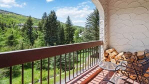 A balcony with a view of a forest and hills, a railing, and stacked firewood. - The Charter at Beaver Creek A220 (Beaver Creek)