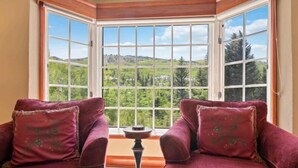 A room with two plush red sofas facing a large window with a view of a forested landscape. - The Charter at Beaver Creek A220 (Beaver Creek)