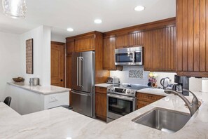 A modern kitchen with wooden cabinets, stainless steel appliances, and a marble countertop.