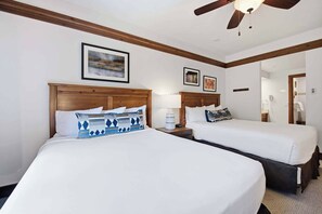 A hotel room with two beds, wooden headboards, and a ceiling fan.