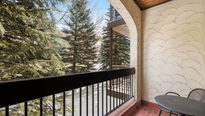 Un balcon avec une table et des chaises, donnant sur un paysage enneigé parsemé de grands arbres à feuilles persistantes.