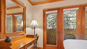 A room with a wooden desk, a chair, a bed, and a lamp. There is a door with a glass panel and a window with a metal grille. - The Charter at Beaver Creek G215 (Beaver Creek)