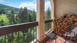 Un balcone con vista su una foresta e una montagna, una pila di legna da ardere e due sedie.