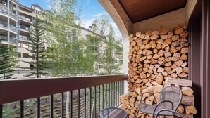A balcony with a stack of firewood, metal chairs, and a view of a residential building. - Charming 2BR Condo at The Charter A330 with Updated Kitchen & Fireplace! (Beaver Creek)