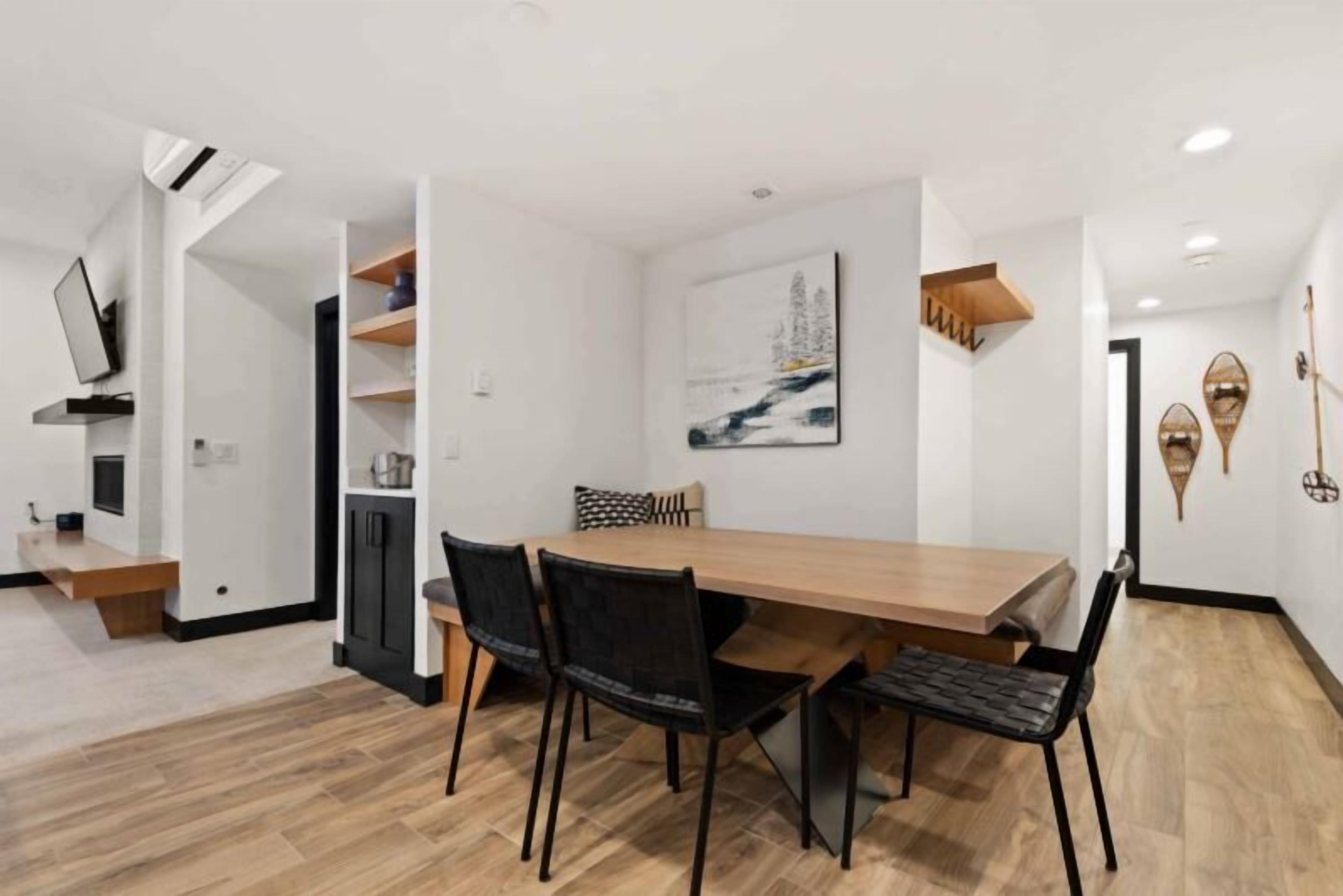 A modern dining area with a wooden table and black chairs, a painting on the wall, and a TV mounted on the wall.