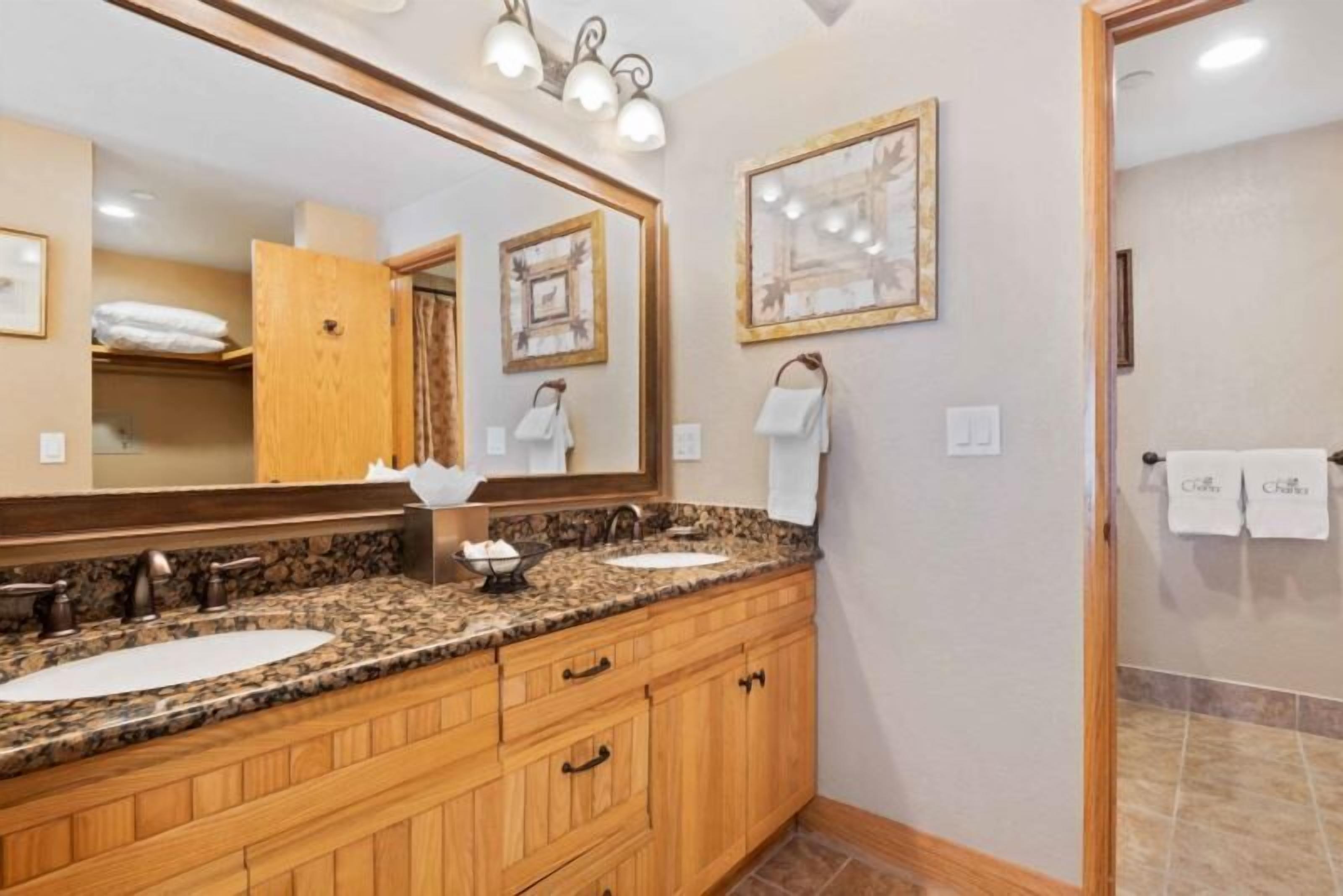 A bathroom with two sinks, wooden cabinets, a large mirror, and wall-mounted lights.