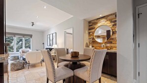 A modern dining area with a round table, four upholstered chairs, and a wooden wall with a round mirror. - The Charter at Beaver Creek A360 (Beaver Creek)