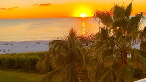 A sunset over a beach with palm trees in the foreground. - Luxurious unit. Sleeps 4. 1.1/2 baths. Beach steps away! (Fort Myers Beach)