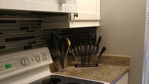 A kitchen with a white stove, a microwave above it, and a backsplash of dark tiles. - Luxurious unit. Sleeps 4. 1.1/2 baths. Beach steps away! (Fort Myers Beach)