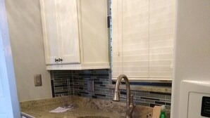 A kitchen with white cabinets, a granite countertop, a stainless steel sink, and a built-in oven. - Luxurious unit. Sleeps 4. 1.1/2 baths. Beach steps away! (Fort Myers Beach)