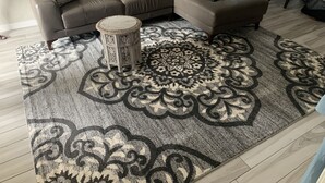 A living room with a sectional sofa, a round side table, and a patterned area rug. - Luxurious unit. Sleeps 4. 1.1/2 baths. Beach steps away! (Fort Myers Beach)