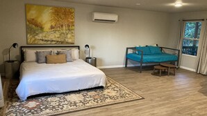 Une chambre à coucher avec un lit, une chaise, un tapis, un climatiseur et une fenêtre avec des rideaux.
