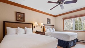Une chambre d’hôtel avec deux lits, des poutres apparentes en bois au plafond, un ventilateur de plafond et une fenêtre donnant sur la forêt.